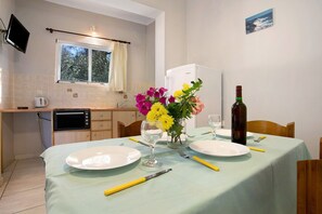 Un coin repas avec une table dressée pour deux personnes, un vase de fleurs, une bouteille de vin et un téléviseur fixé au mur.