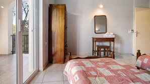 Un dormitorio con una cama, un armario de madera, una mesita de noche con un espejo y una puerta que da a un balcón.