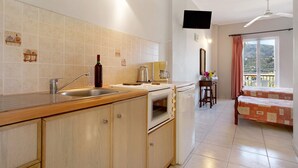 Een keuken met een spoelbak, fornuis en oven, een eethoek met een tafel en stoelen, en een balkon met uitzicht.