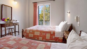 Een slaapkamer met twee bedden, een kaptafel, een spiegel en een raam met uitzicht op bomen.