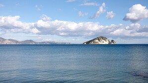 Een rustige zee met een afgelegen eiland en bergen onder een heldere lucht.