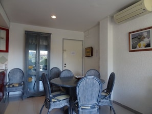 A dining area with a round table and six chairs, a cabinet with glass doors, and an air conditioning unit on the wall.