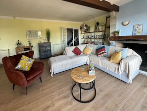 Een woonkamer met een bank, fauteuil en salontafel, een boekenkast en een open haard.