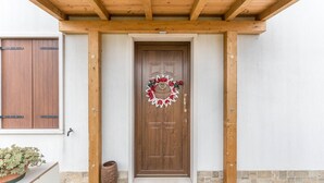 Une porte en bois ornée d’une guirlande, un paillasson et un pot de fleurs.