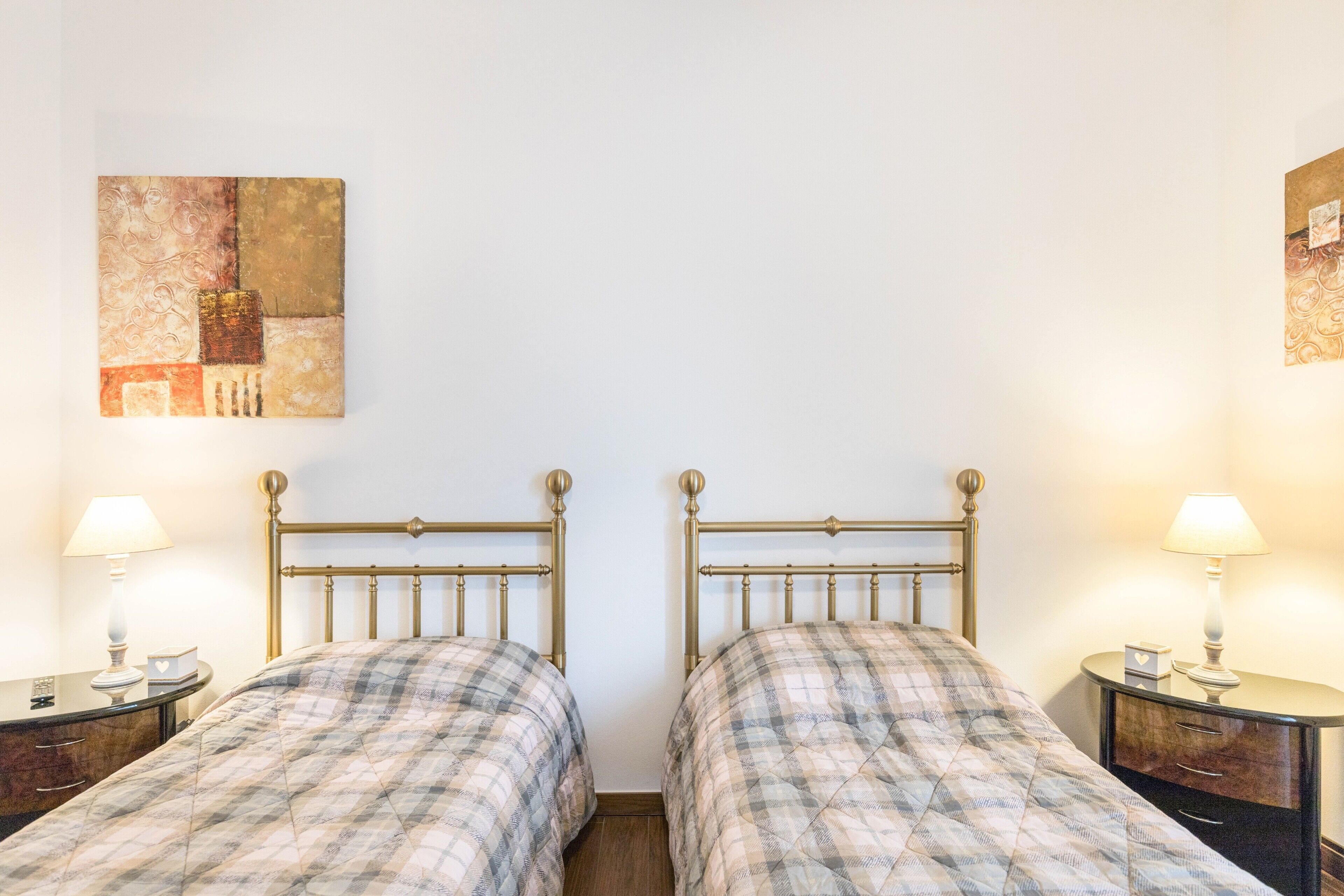 A room with two beds, each with a headboard, bedside tables, and lamps.