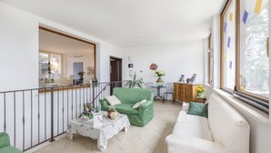 Un grand salon comprenant un canapé vert, un canapé blanc et une petite table sur laquelle est posé un vase de fleurs.