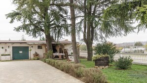 Un bâtiment avec une porte de garage verte, une terrasse en briques et un petit jardin agrémenté d’arbres et d’arbustes.