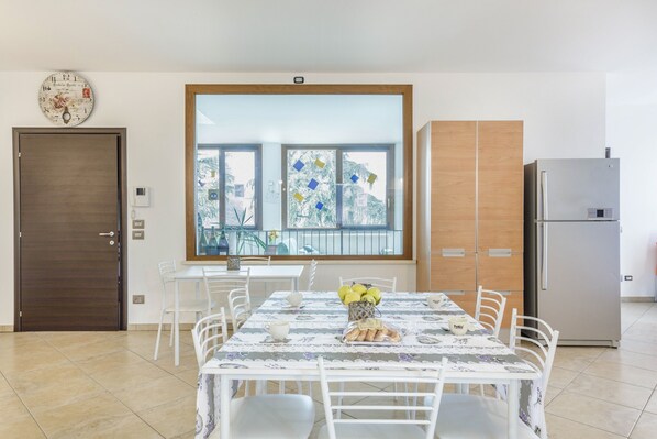 A dining area with a table set for four, a refrigerator, a wooden cabinet, and a large window with a view.