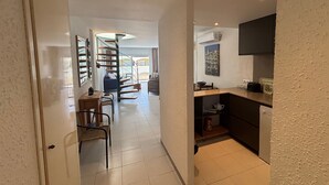 A hallway leading to a living area with a spiral staircase, a kitchen area with a flat-screen TV, and a dining area with a blue sofa. - Holiday Apartment "Mar D'or 223" with Shared Pool, Terraces & Wi-Fi (girona)