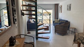 A modern interior with a spiral staircase, a dining area, a sofa, and a wicker chair. - Holiday Apartment "Mar D'or 223" with Shared Pool, Terraces & Wi-Fi (girona)