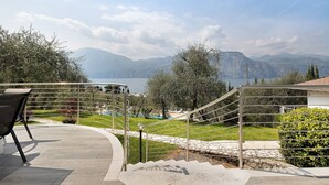 Un balcón con vistas a montañas y un lago, una escalera y mobiliario exterior.