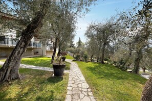 Un chemin de pierres qui traverse un jardin, avec des arbres et un bâtiment en arrière-plan.