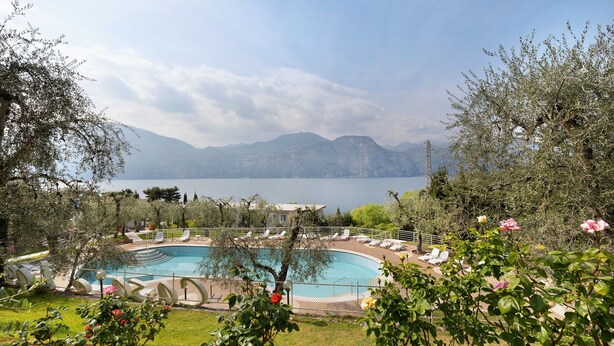 Una piscina con sillones de descanso, rodeada de vegetación y con montañas al fondo.