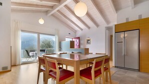 Una cocina moderna con un refrigerador grande, una mesa de comedor de madera con sillas rojas y vistas a través de la puerta de cristal.