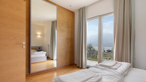Una habitación de hotel moderna con un espejo grande, una cama con ropa blanca impecable, una puerta corredera y vistas al exterior.