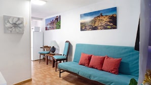 Une pièce avec un canapé de couleur turquoise, des coussins rouges, une table basse en bois, une chaise et deux tableaux accrochés au mur.