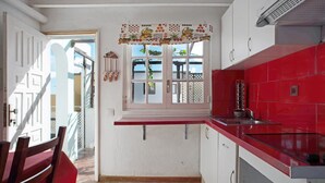 Une cuisine avec un plan de travail rouge, des armoires blanches et une fenêtre agrémentée d’une lambrequin décorative.