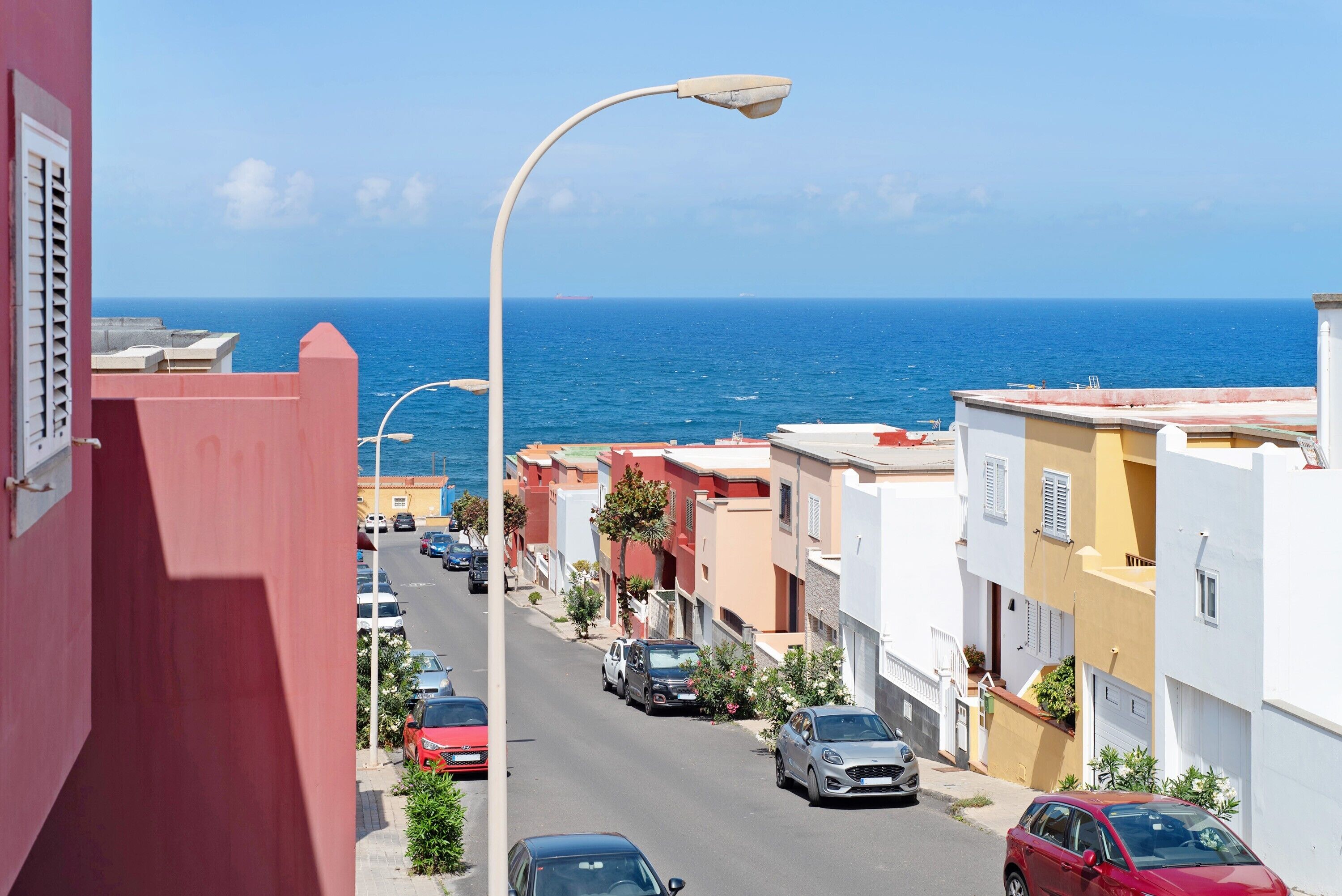 Eine Küstenstraße mit parkenden Autos, Gebäuden und freiem Blick auf das Meer.