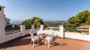 A terrace with white metal chairs and a table, overlooking a scenic landscape with trees and a distant view of the sea. - "Villa with private swimming pool" with Sea View, Private Terrace & Wi-Fi (Mijas Pueblo)