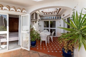 An open patio with a table and chairs, a potted plant, and a door leading to a room.