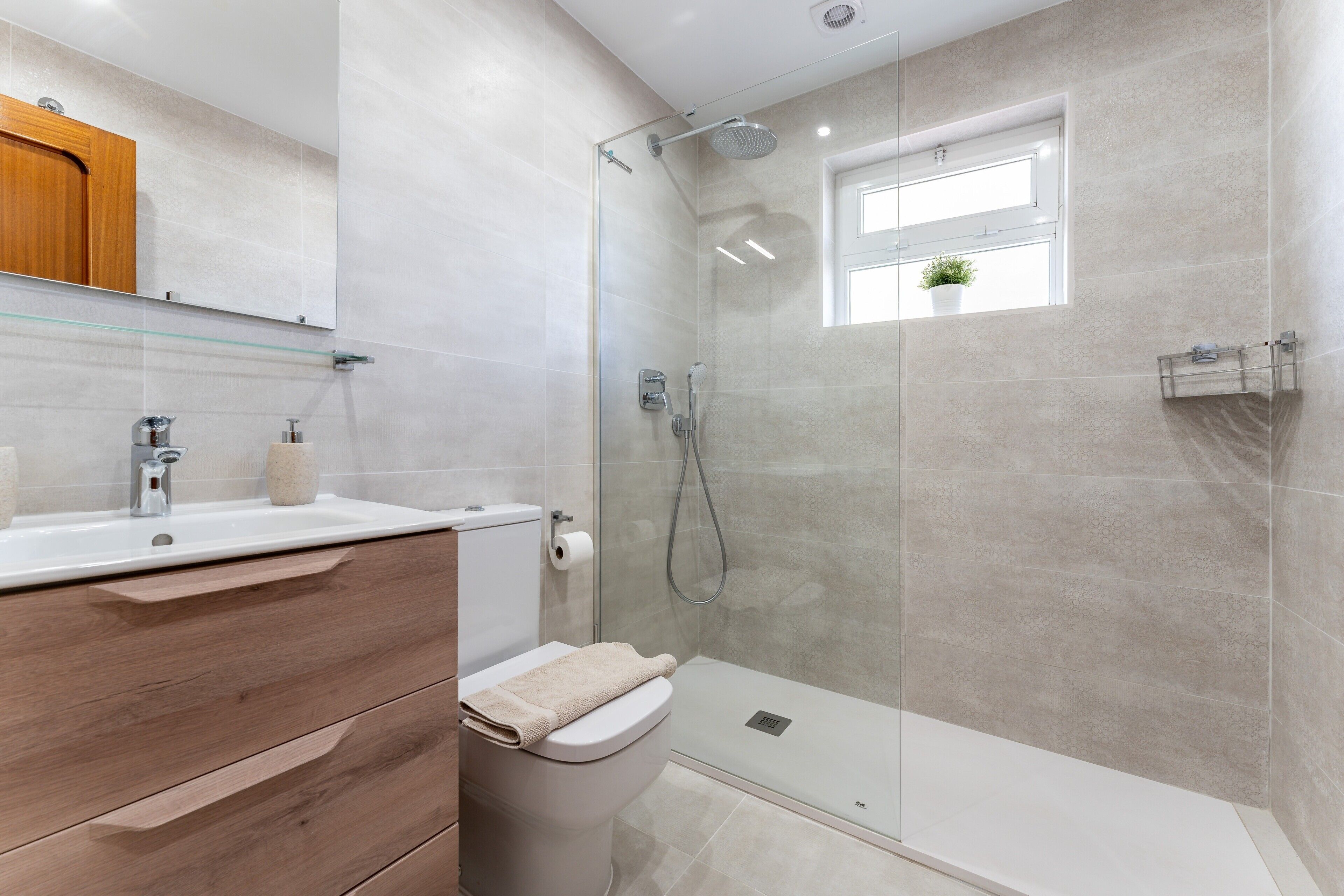 Un baño moderno con cabina de ducha de vidrio, inodoro, lavabo y tocador de madera.