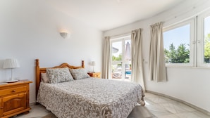 A bedroom with a bed, bedside tables, a lamp, a window with curtains, and a view of the outside. - "Villa with private swimming pool" with Sea View, Private Terrace & Wi-Fi (Mijas Pueblo)
