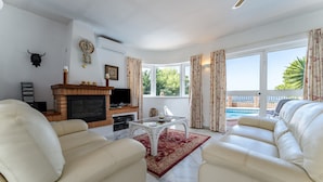 A living room with a fireplace, leather sofas, a coffee table, and a view of a pool. - "Villa with private swimming pool" with Sea View, Private Terrace & Wi-Fi (Mijas Pueblo)