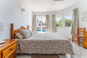 A bedroom with a bed, wooden nightstand, lamp, and a view of a swimming pool.