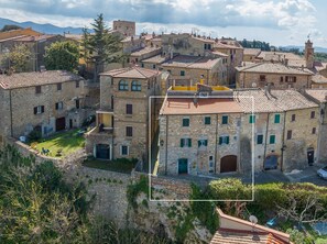 A historic stone building with multiple windows, a courtyard, and a view of the surrounding village.