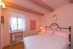 A bedroom with a bed, a window with curtains, a bedside table with a lamp, and a wall-mounted picture.