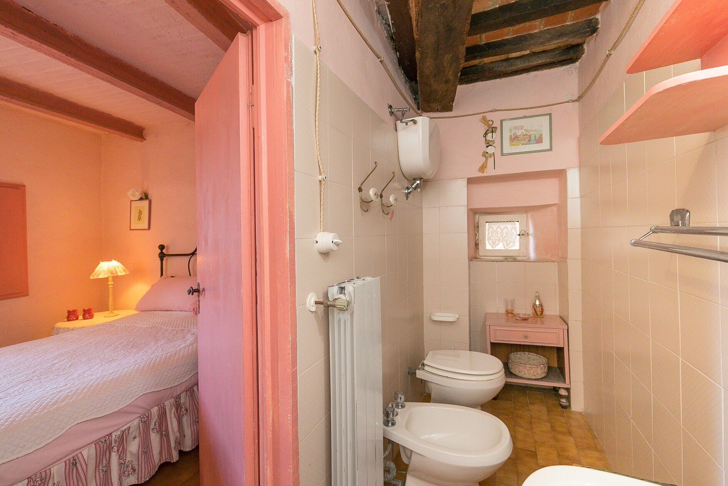 A bedroom with a bed, a bedside table with a lamp, and a pink door.