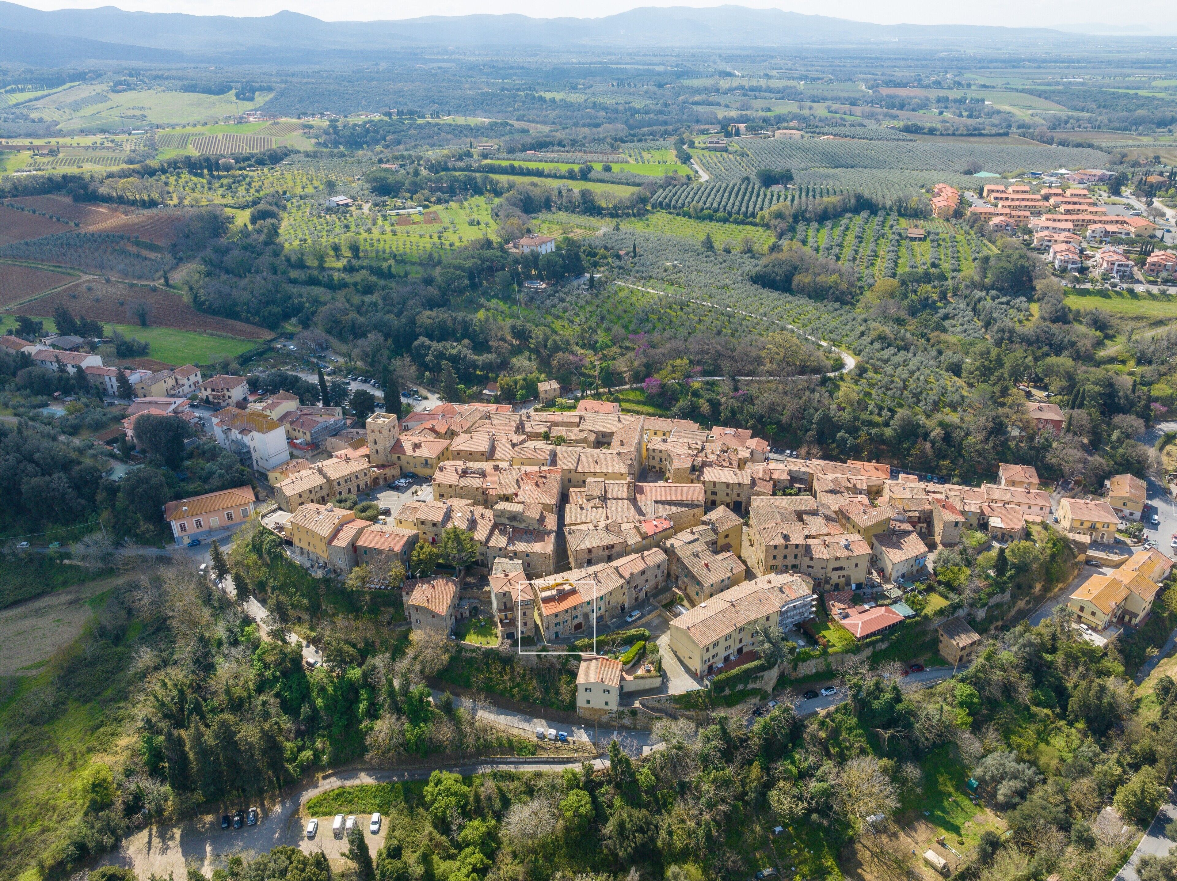 An aerial view of a historic town with dense architecture, surrounded by agricultural fields and rolling hills.