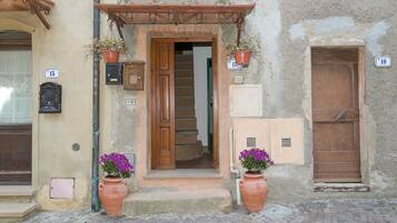 Un bâtiment avec une porte en bois, portant le numéro 17, et un escalier menant à l’intérieur. On peut voir deux pots en terre cuite ornés de fleurs sur les marches.