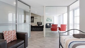 Et moderne hotelværelse med seng, sofa, rød stol og glasvæg.