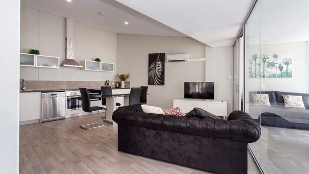 Et moderne køkken med indbyggede apparater, et spiseområde med en sort sofa og en stue med et stort fjernsyn samt en sofa.
