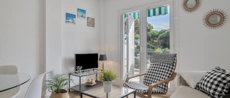 Een moderne woonkamer met een glazen tafel, een televisie, een geruit fauteuil en een bank.