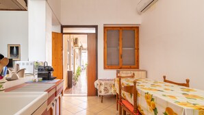 A compact kitchen with a refrigerator, stove, and sink. A dining table with chairs is positioned near a window with a wooden frame.