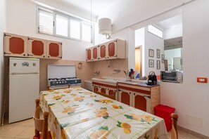 Una cocina compacta con refrigerador, estufa, lavamanos y una mesa de comedor con mantel estampado de frutas.