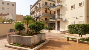 A courtyard with a bench, potted plants, and a building with balconies.