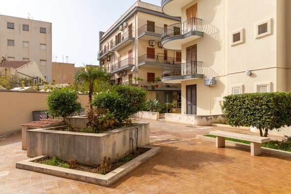 A courtyard with a bench, potted plants, and a building with balconies.