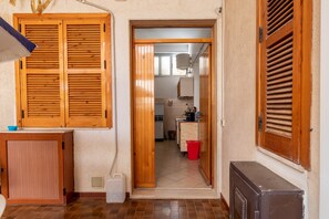 A hallway with wooden doors, a kitchen in the background, and a red trash bin.