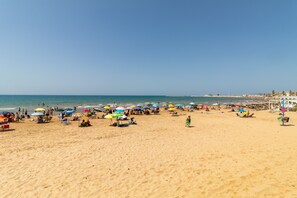 A beach with numerous umbrellas and beach chairs, a clear sky, and a calm sea.