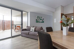 Een moderne woonkamer met een bank, een eettafel en stoelen. Er is een glazen schuifdeur die leidt naar een buitenruimte.