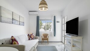 A modern living room with a sofa, a television on a white stand, a wicker chair, and a patterned rug.