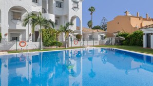 A swimming pool with a clear blue water surface, surrounded by a white building with balconies and palm trees.