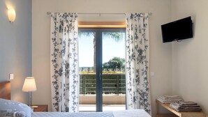 Un dormitorio con cama, mesita de noche, lámpara, televisor y balcón con cortinas.