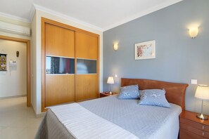 A bedroom with a bed, bedside lamps, a nightstand, a wooden wardrobe, and a wall-mounted picture.