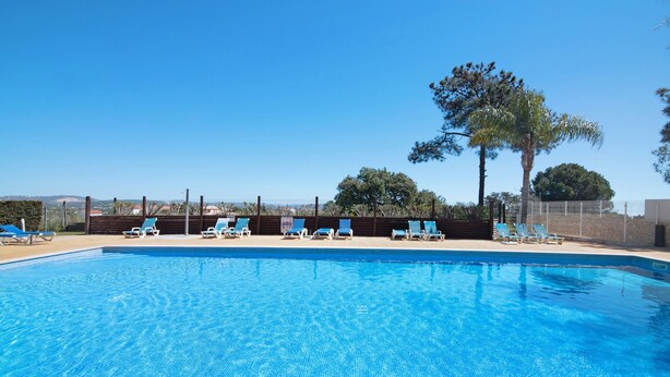 Una piscina azul cristalina con sillas de descanso y una valla de madera.