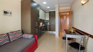 Una habitación de hotel compacta con kitchenette, zona de comedor y sofá con cojines estampados.