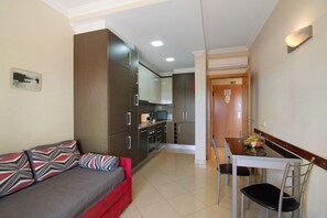 A compact hotel room with a kitchenette, a dining area, and a sofa with patterned cushions.
